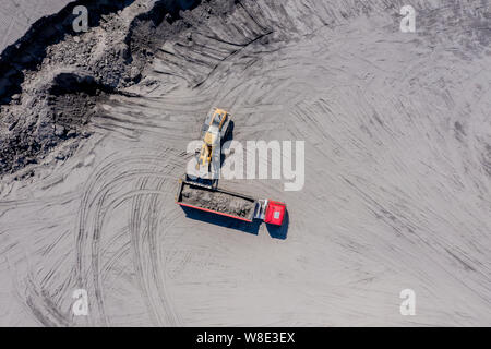 Luftbild des Baggers gießt Sand in den Wagen. Auf der Baustelle Ansicht von oben. Schießen von der Drohne. Stockfoto