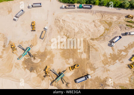 Luftbild des Baggers gießt Sand in den Wagen. Auf der Baustelle Ansicht von oben. Schießen von der Drohne. Stockfoto