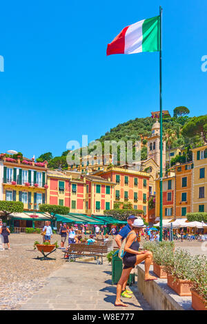 Portofino, Italien - 1. Juli 2019: Italienische Flagge auf dem hohen Fahnenmast und Waterfront mit wandern Menschen in Portofino - Famous Resort auf dem Italienischen rivi Stockfoto