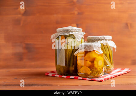 Gläser von eingelegtem Gemüse: Gurken, Tomaten, Auberginen mit rustikalen Holzmöbeln Hintergrund. Marinierte und Konserven. Stockfoto