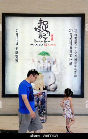 Menschen gehen vorbei an einem Plakat des Films 'Monster Jagd" und ein Modell der Wuba, ein Charakter des Films in einem Kino in Shanghai, China, 26. Juli 2015. Th Stockfoto