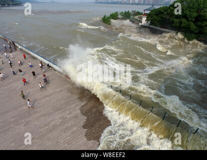 Besucher und Anwohner wie Wellen aus einem Tidal Bore Schwankung hinter einer Barriere am Ufer des Qiantang Fluss in Hangzhou City, East China Zhejian Stockfoto