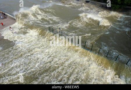 Besucher und Anwohner wie Wellen aus einem Tidal Bore Schwankung hinter einer Barriere am Ufer des Qiantang Fluss in Hangzhou City, East China Zhejian Stockfoto