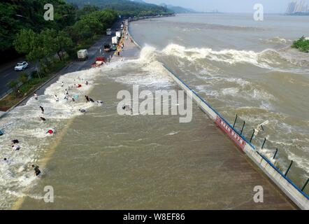 Besucher und Anwohner wie Wellen aus einem Tidal Bore Schwankung hinter einer Barriere am Ufer des Qiantang Fluss in Hangzhou City, East China Zhejian Stockfoto