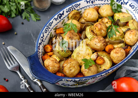 Junge gebackene Kartoffeln mit Zucchini, Karotten, grüne Bohnen, in eine keramische Form entfernt, vor einem dunklen Hintergrund, horizontale Ausrichtung, close-up Stockfoto