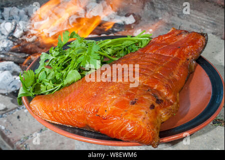 Die Platte von geräuchertem Lachs auf dem Holzkohlegrill mit dem Verbrennen von Kohle im Hintergrund Stockfoto