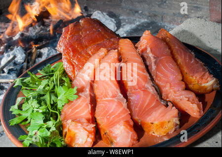 Die Platte von geräuchertem Lachs auf dem Holzkohlegrill mit dem Verbrennen von Kohle im Hintergrund Stockfoto