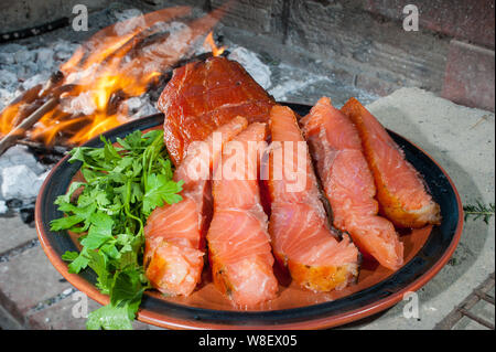 Die Platte von geräuchertem Lachs auf dem Holzkohlegrill mit dem Verbrennen von Kohle im Hintergrund Stockfoto