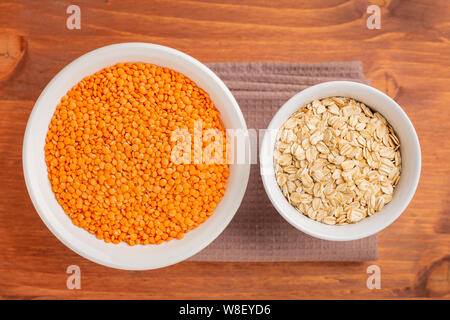 Gesunde Ernährung, Diäten, Ernährung, vegan Protein Quelle. Raw von Leguminosen, rote Linsen, eiche Flocken in die weiße Schalen. Ansicht von oben mit der Kopie Raum Stockfoto