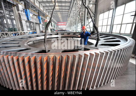 ---- Ein chinesischer Arbeiter leitet ein Kran die riesigen Zahnkranz der Fräsmaschine in einem Werk von Citic Heavy Industries Co., Ltd. in Luoyang ci zu heben Stockfoto