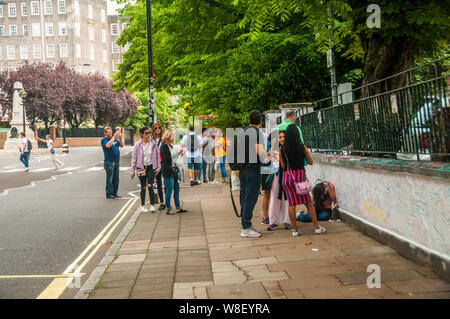 Touristen mit dem Graffiti an den Wänden außerhalb der Abbey Road Studios in London mit der berühmten Kreuzung hinter sich. Stockfoto