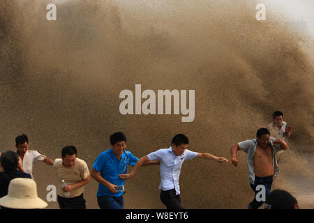 Besucher und Anwohner laufen weg wie Wellen aus einem Tidal Bore Schwankung hinter einer Barriere am Ufer des Qiantang Fluss in Hangzhou City, East China Zh Stockfoto