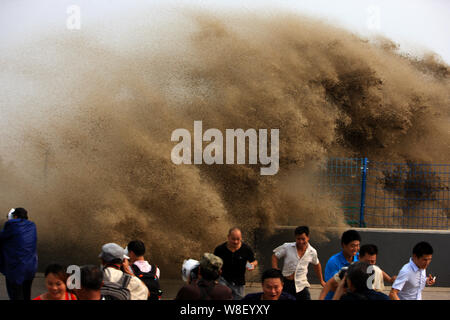 Besucher und Anwohner laufen weg wie Wellen aus einem Tidal Bore Schwankung hinter einer Barriere am Ufer des Qiantang Fluss in Hangzhou City, East China Zh Stockfoto