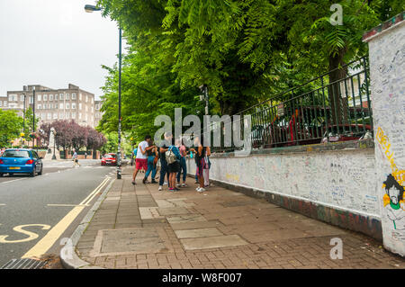 Touristen mit dem Graffiti an den Wänden außerhalb der Abbey Road Studios in London mit der berühmten Kreuzung hinter sich. Stockfoto