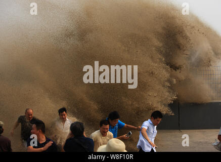 Besucher und Anwohner laufen weg wie Wellen aus einem Tidal Bore Schwankung hinter einer Barriere am Ufer des Qiantang Fluss in Hangzhou City, East China Zh Stockfoto