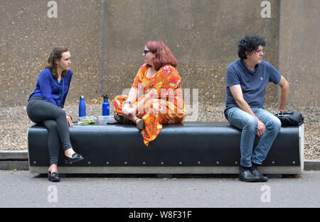 London, England, UK. Zwei Frauen und ein Mann auf einer Bank durch die Tate Modern Galerie, Bankside sitzen Stockfoto