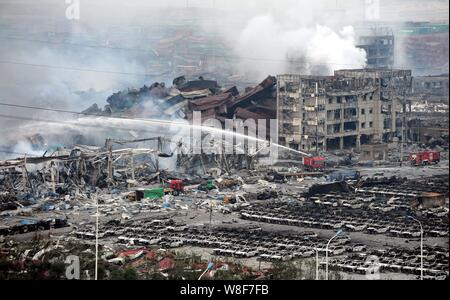 Chinesische Feuerwehrmänner Schlauch Wasser Feuer neben verbrannten Autos und Rückstände von Gebäuden und Container von den tödlichen Explosionen in Bi verwüstet zu löschen Stockfoto