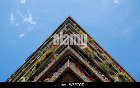 Wohnungen errichtet in der Nachkriegszeit Brutalist architektonischen Stil im Barbican in der City von London, mit bunten Blumen auf dem Balkon. Stockfoto