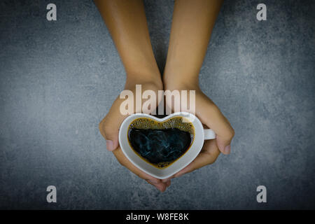 Hand, die Herzform Tasse Kaffee auf konkreten Hintergrund Stockfoto