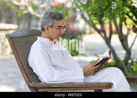 Senior Mann liest ein Buch im Garten Stockfoto