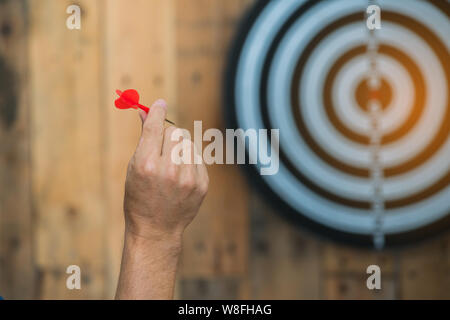 Hand halten roten dart Pfeil bereit zu schlagen in der Zielgruppe, Dartscheibe auf Holz Stockfoto