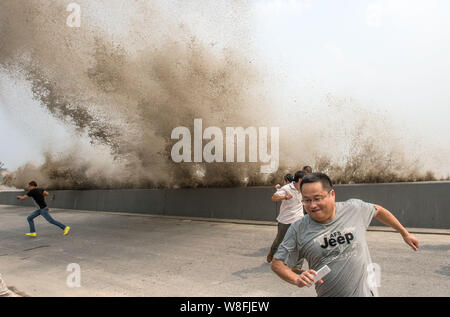Besucher und Anwohner laufen weg wie Wellen aus einem Tidal Bore Schwankung hinter einer Barriere am Ufer des Qiantang Fluss in Hangzhou City, East China Zh Stockfoto