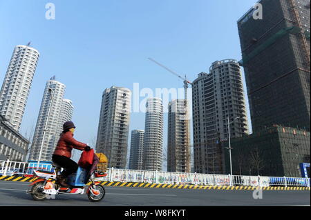 ---- Ein chinesischer Radfahrer reitet ihr Elektrofahrrad vorbei an der Baustelle für eine Wohn- Projekt in Rizhao, East China Shandong p Stockfoto