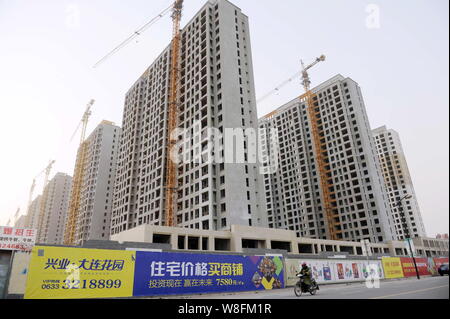 ---- Ein chinesischer Radfahrer fährt mit dem Elektrofahrrad Vergangenheit neue High-rise apartment Gebäude in eine Wohn- Projekt im Bau in Rizha Stockfoto