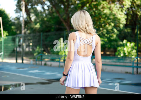 Junge schlanke Frau mit einem sportlichen Körper, lange blonde Haare, in einem rosa Sport Kleid, führt eine Übung auf dem Sportplatz in der Natur Stockfoto