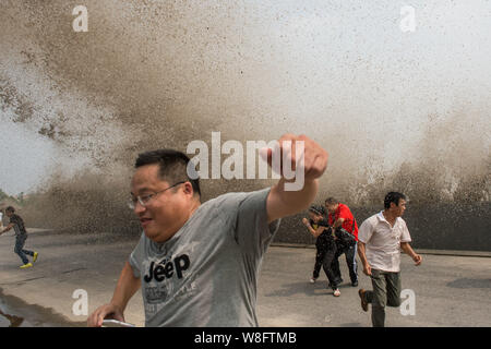 Besucher und Anwohner laufen weg wie Wellen aus einem Tidal Bore Schwankung hinter einer Barriere am Ufer des Qiantang Fluss in Hangzhou City, East China Zh Stockfoto