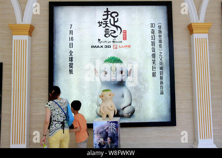 Menschen gehen vorbei an einem Plakat des Films 'Monster Jagd" und ein Modell der Wuba, ein Charakter des Films in einem Kino in Shanghai, China, 26. Juli 2015. Th Stockfoto