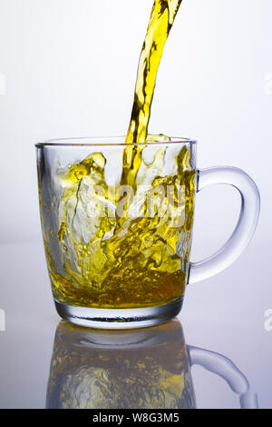 Hell gelber Tee ist in einer klaren Stein gegossen. Gelb Jet auf einem weißen Hintergrund. Flüssigkeit in einem transparenten Behälter Stockfoto