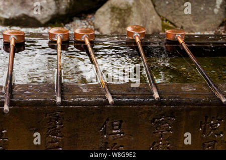 Kupferlöffel und japanisches Steinwasserbecken mit geätzten japanischen Schriftzeichen in Kamakura, Japan. Stockfoto