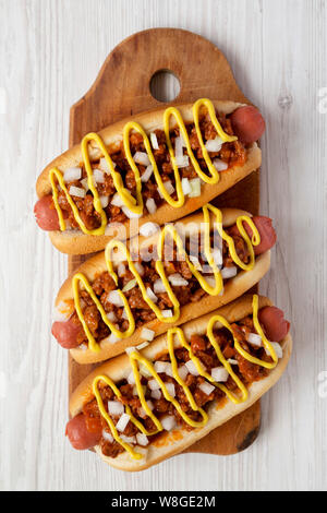 Hausgemachte Coney Island Chili Dog mit Zwiebeln und Senf auf einer rustikalen Holzbrett auf weißem Holz- Hintergrund, Ansicht von oben. Flach, Overhead, von oben Stockfoto