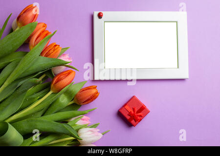 Leeren Bilderrahmen neben einem Blumenstrauß aus Tulpen und roter Geschenkbox Stockfoto