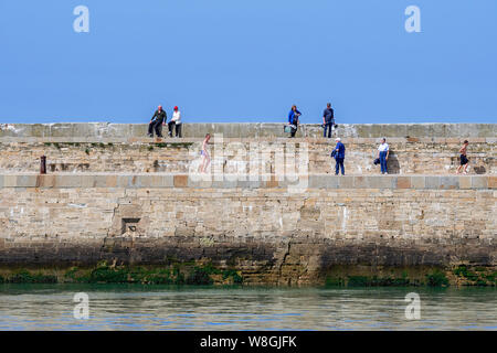 Touristen zu Fuß auf alten Seedeich/Sea Wall im Hafen von Port-en-Bessin-Huppain entlang des Ärmelkanals, Calvados, Normandie, Frankreich Stockfoto