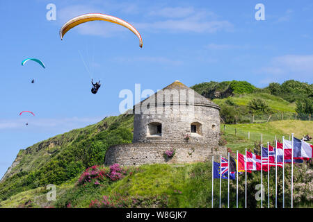 Fliegen/hochfliegende Gleitschirme oberhalb des 17. Jahrhunderts Tour Vauban Turm in Port-en-Bessin-Huppain entlang des Ärmelkanals, Calvados, Normandie, Frankreich Stockfoto