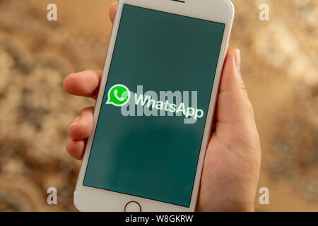 Weibliche hand mit Apple Handy mit Logo von social media WhatsApp auf dem Bildschirm. Social media Symbol. Kann als Illustration oder Marketing Konzept verwendet werden. Stockfoto