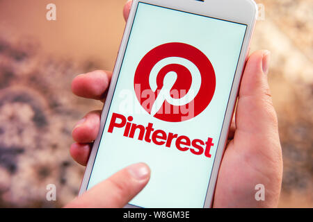 Weibliche hand mit Apple Handy mit Logo von social media Pinterest auf dem Bildschirm. Social media Symbol. Kann wie Marketing oder Business Konzept verwendet werden. Stockfoto