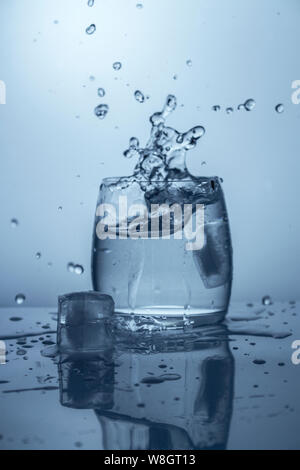 Spritzen der Wasserspritzer fallen ein Stück Eis transparente Glas Wasser Stockfoto