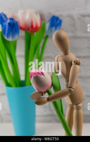 Holz- Mann mit einem hölzernen rosa Blume. Ein Mann mit einer Blume, Tulpen in seine Hände, ein Konzept für ein Datum mit seinem Geliebten wartet. Künstliche Holz- m Stockfoto