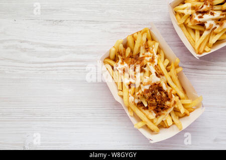 Fastfood: Pommes Frites mit Käsesoße und gebratene Zwiebel in Papier kartons auf einer weißen Holz- Hintergrund, Ansicht von oben. Platz für Text. Stockfoto