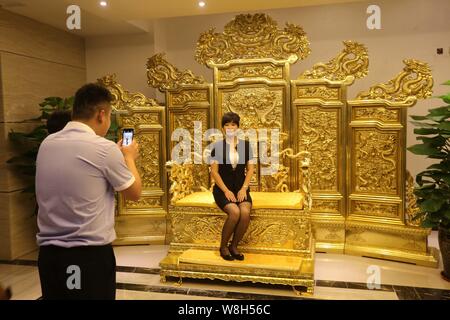 Ein chinesischer Mitarbeiter Posen für Fotos durch das Sitzen auf dem Gold Replik der Stuhl des Kaisers in die verbotene Stadt in der Lobby eines Hotels in Weifang Stadt Stockfoto