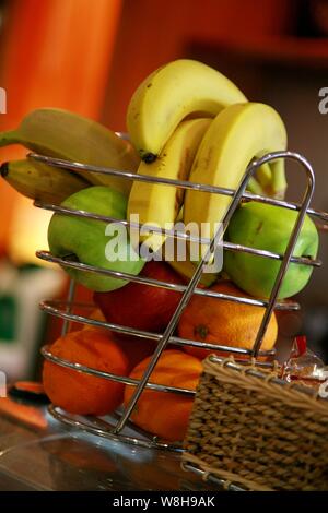 Frisches Obst, einschließlich Bananen, Äpfel und Orangen, in einem Korb auf einer Küchentheke angeordnet, um eine gesunde Ernährung zu fördern Stockfoto