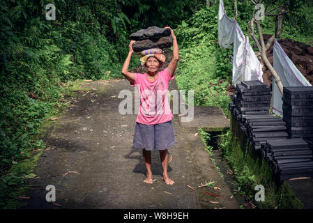 BALI, Indonesien - Januar 9, 2018: Balinesische Frau arbeitet hart an der Gewinnung von Naturstein in Bali, trägt sie mit Steinen aus dem Steinbruch auf dem Kopf Stockfoto