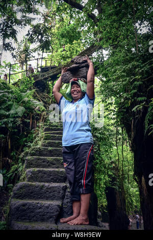 BALI, Indonesien - Januar 9, 2018: Balinesische Frau arbeitet hart an der Gewinnung von Naturstein in Bali, trägt sie mit Steinen aus dem Steinbruch auf dem Kopf Stockfoto