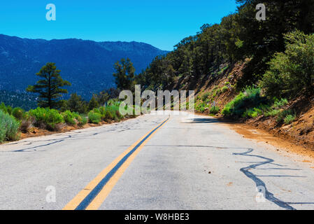 Schmale gerade Asphaltstraße mit gelben Linien, die Hügel in Richtung Berge unter strahlend blauen Himmel. Stockfoto