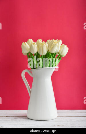 Blumenstrauß aus den weißen Tulpen in weiss emailliert Kanne auf rosa Hintergrund Stockfoto
