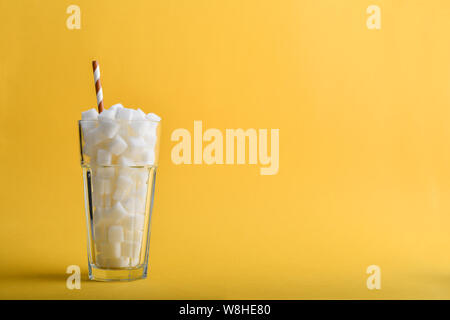 Glas voll Würfelzucker mit Getränk Stroh auf gelbem Hintergrund - ungesunde Ernährung Konzept. Stockfoto
