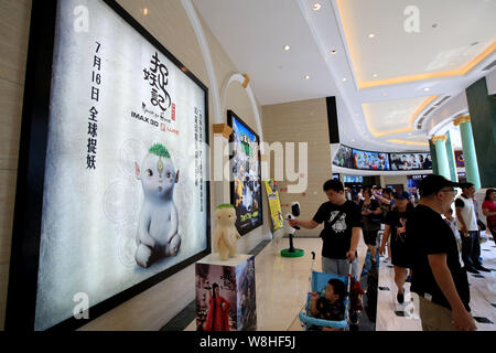 Menschen gehen vorbei an einem Plakat des Films 'Monster Jagd" und ein Modell der Wuba, ein Charakter des Films in einem Kino in Shanghai, China, 26. Juli 2015. Th Stockfoto